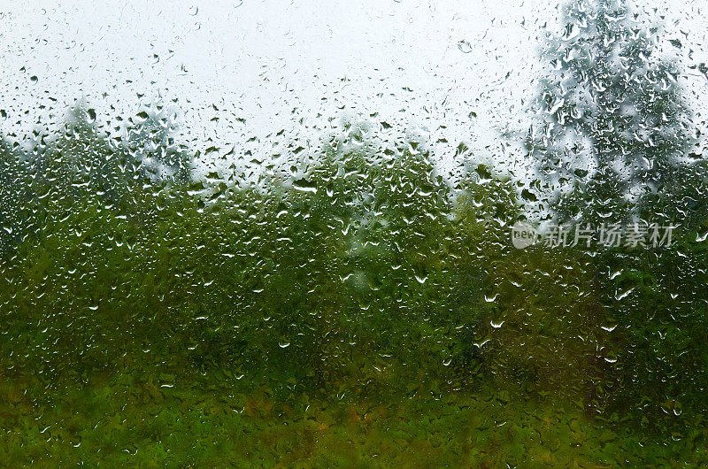 景观和多云的天空透过水滴雨潮湿的窗户