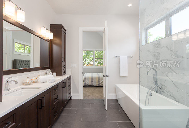 主浴室内部在豪华的家大镜子，淋浴，和浴缸。包括深色硬木橱柜和瓷砖地板。的卧室