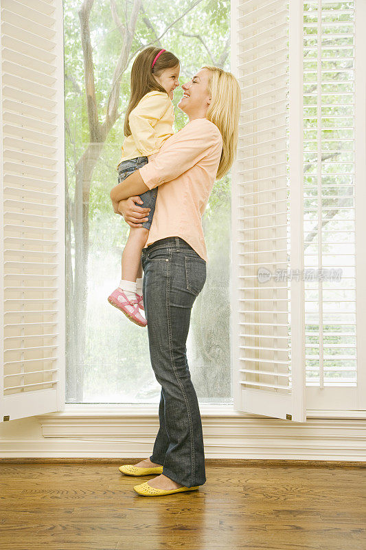母亲抱着女儿站在打开的窗户前