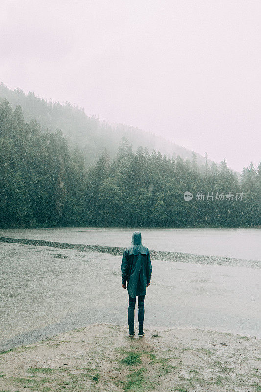 在倾盆大雨中，穿着雨衣的人站在湖边