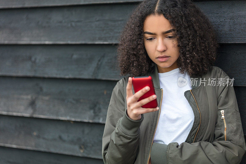 室外肖像美丽的悲伤沮丧的混合种族非洲裔美国女孩少女女年轻女人发红色手机穿绿色飞行员夹克