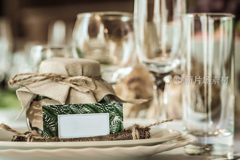 在漂亮舒适的餐厅里为婚礼庆典设置的质朴的餐桌。酒杯，盘子和桌上的食物。客人们在一个质朴的罐子里互相补充。带有文本空间的漂亮卡片