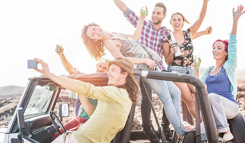 一群快乐的朋友在沙漠上敞篷吉普车聚会-旅行的人有乐趣喝香槟和自拍-友谊和度假概念-关注男人的脸与手机