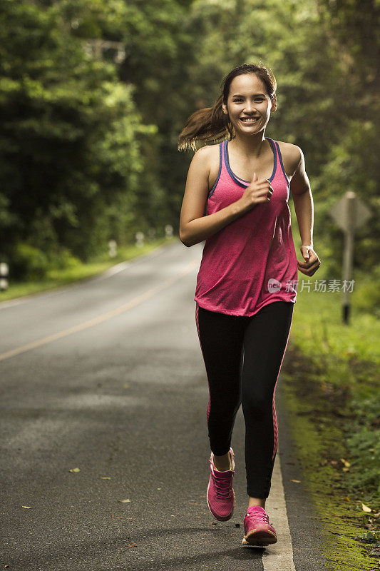 一个亚洲女人在阳光明媚的森林里的路上慢跑