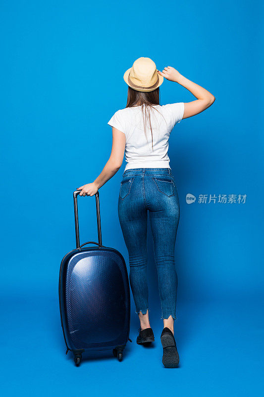 后视图行走的女人与手提箱。美丽的女孩在动。带行李的旅行者的背面视图在蓝色背景上孤立。