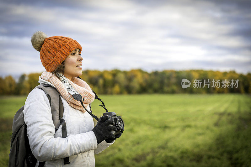 美丽的年轻女子与数码相机照片在日落