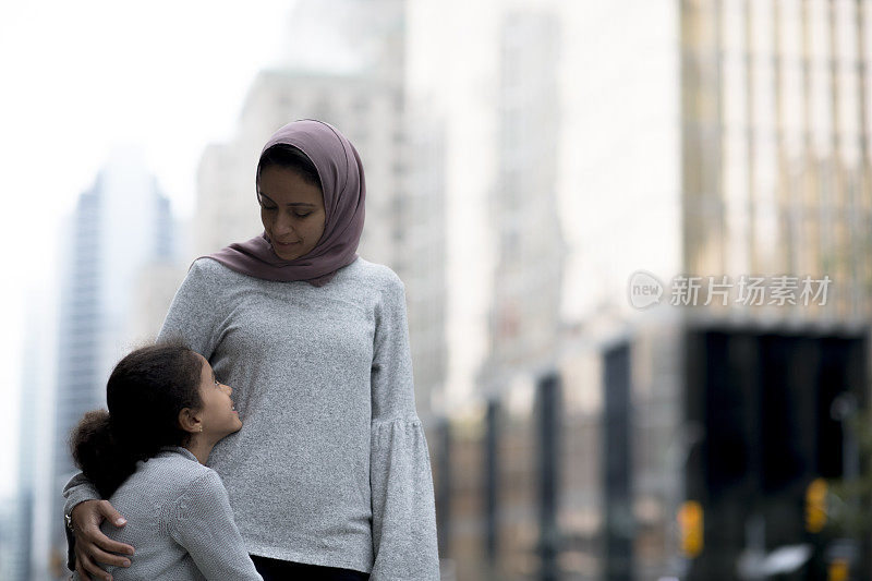 穆斯林母亲拥抱和微笑她的女儿在城市