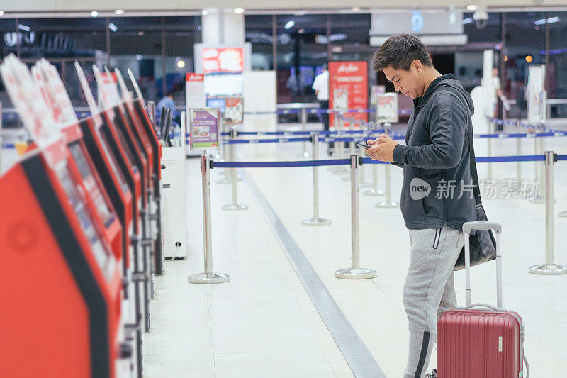 年轻亚洲旅客在机场离港大厅的自助值机处。