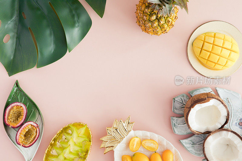 淡粉色背景的异国水果-菠萝，芒果，椰子，杨桃，百香果。俯视图和平放