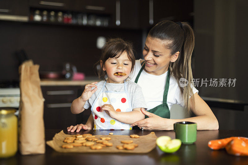 快乐的家庭与烤饼干，母亲和女儿有乐趣和吃新鲜热饼干