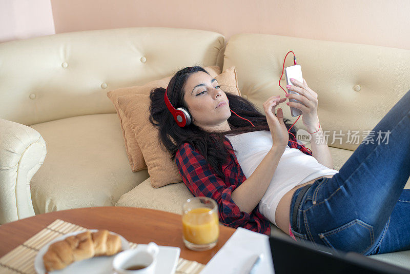 快乐的女孩躺在沙发上，用手机听音乐