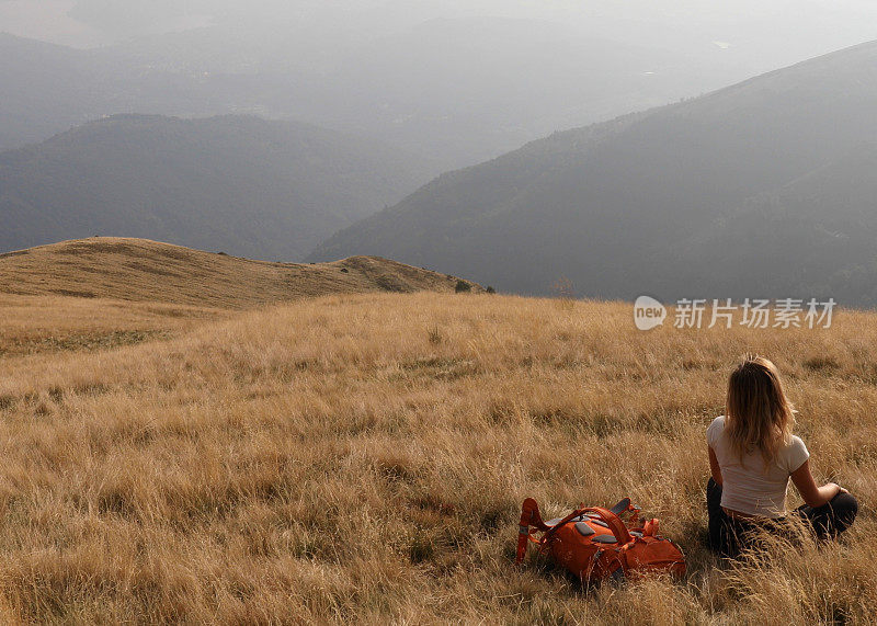 女徒步旅行者坐在长满草的山坡上