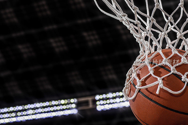 一个篮球从网里掉下来的特写，背景是竞技场的灯光