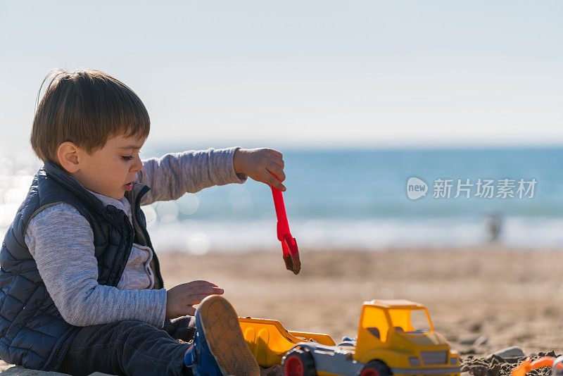 男孩在海滩上玩玩具卡车