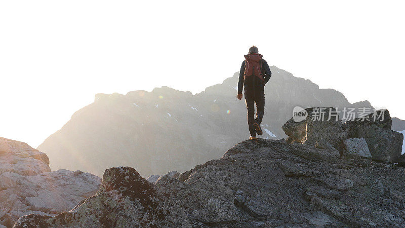 登山者在日出时徒步爬上岩石的顶峰