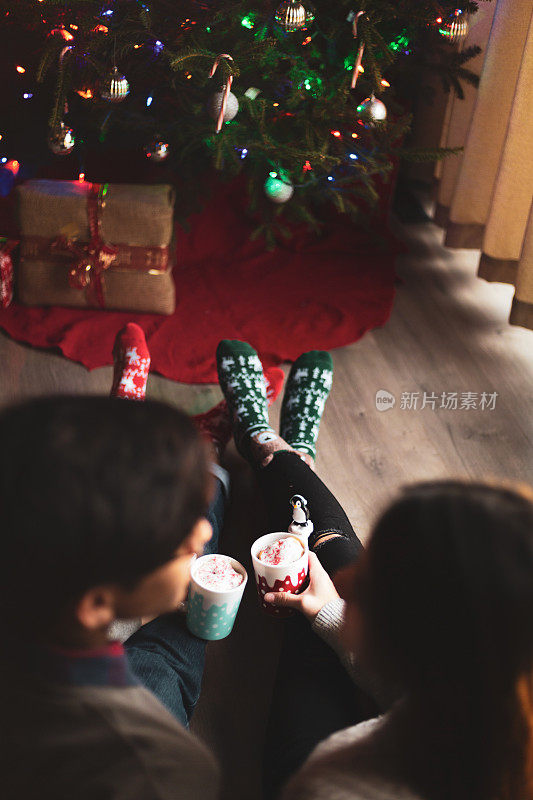 年轻夫妇坐在圣诞树前喝热巧克力