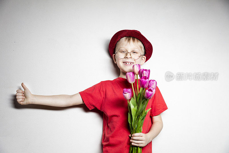 男孩拿着粉红色的郁金香花开心地笑着做ok手势，用手指竖起大拇指，很棒的手势