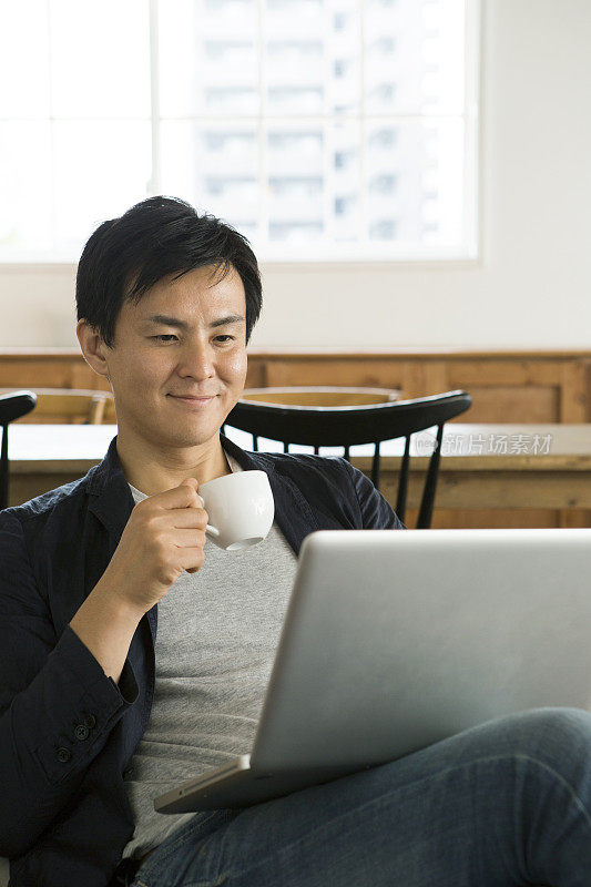 微笑的中年男子在沙发上使用笔记本电脑