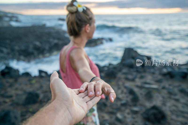 日出时在岩石海岸线上牵着手的夫妇，跟我来