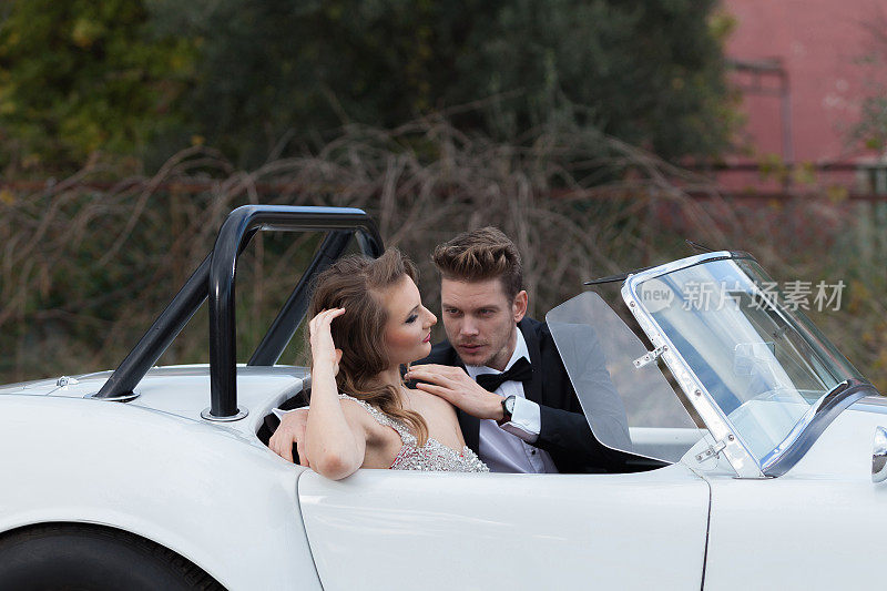 一对优雅的年轻夫妇坐在白色老爷车旁