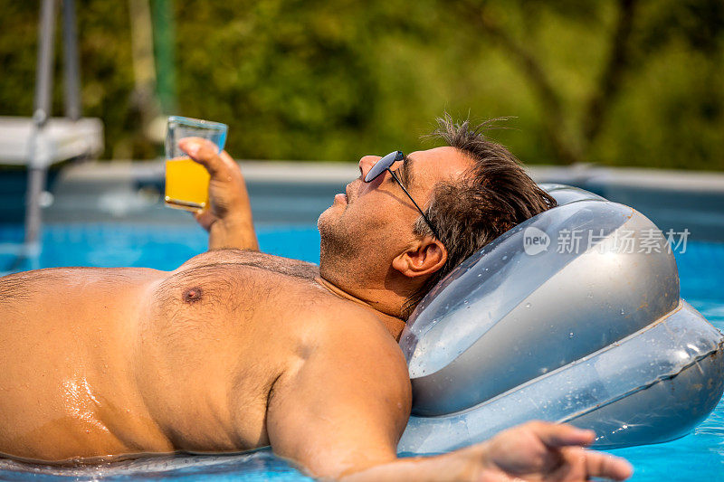 在充气床垫上戴着太阳镜的成熟微笑男人。游泳池里的胖子