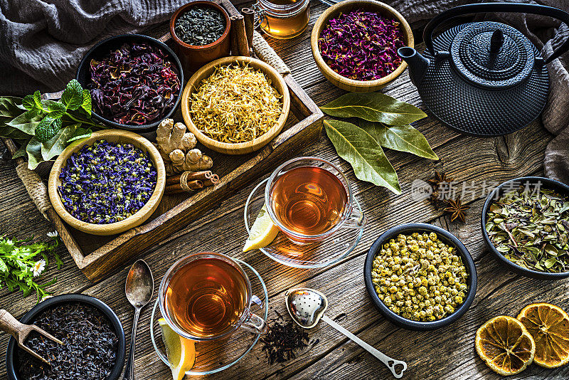 花草茶:两杯茶，各种各样的干茶叶和鲜花从上面拍摄在质朴的木桌
