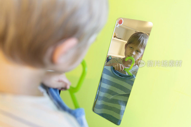 7岁的小男孩看着镜子，拆开自己的衣服。在冠状病毒大流行期间呆在家里。