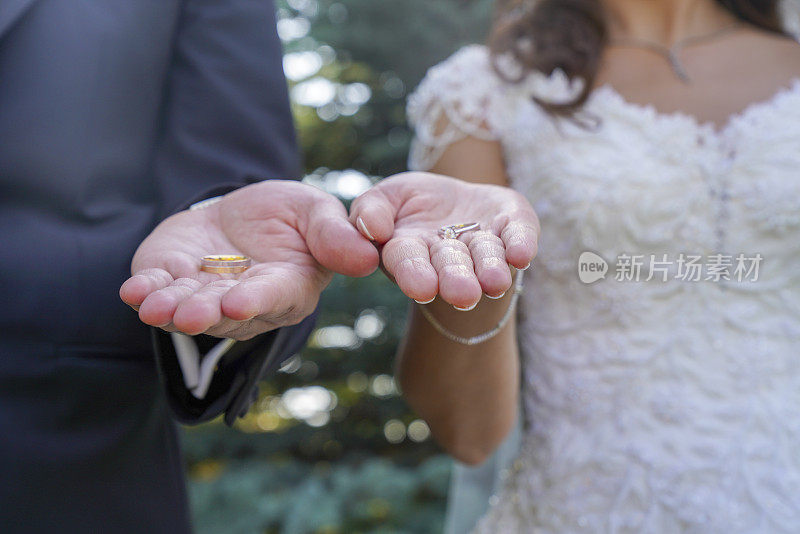 新婚夫妇手中手持两枚结婚戒指金的结婚戒指一男一女结婚典礼上手持一枚贵重金属的结婚戒指。