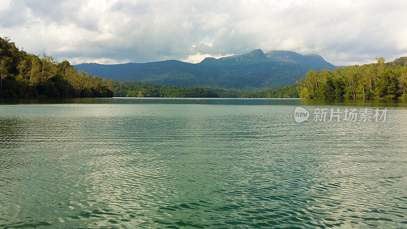 一个湖泊与绿色的水和绿色的树和山的背景与多云的天空的风景图像。绿色色调。Neyyar野生动物保护区。