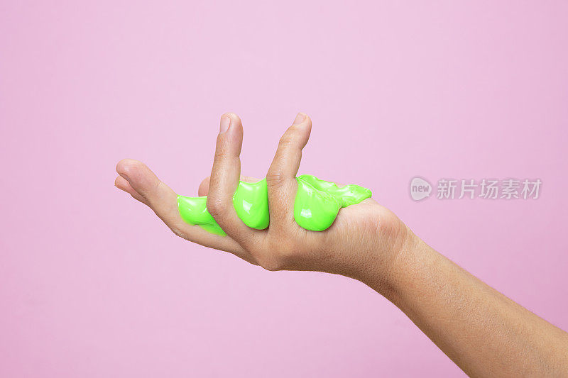 手与霓虹灯绿色黏液玩具粉红色波普艺术背景。