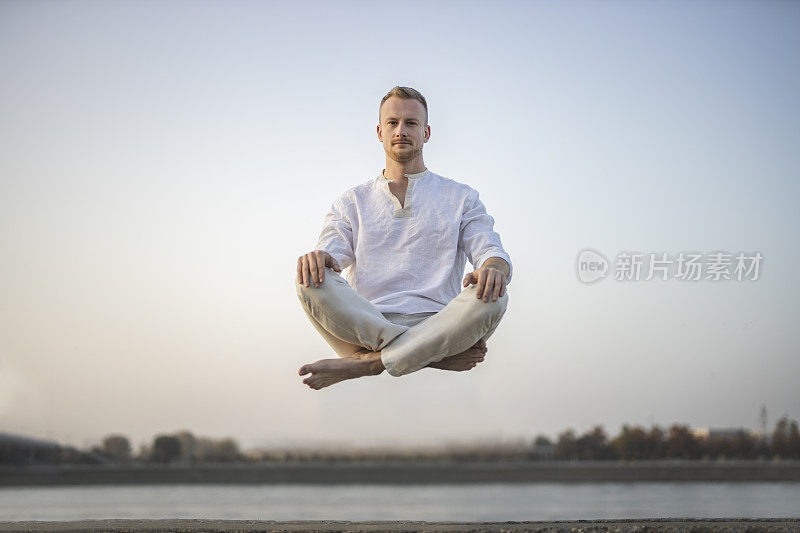 年轻美丽的男子在半空中沉思的肖像，漂浮在户外地面上，坐在莲花姿势，莲花身