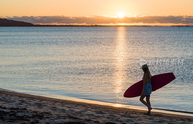 澳大利亚女性冲浪在海滩上日落