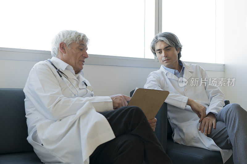 成人和资深医生在看医生办公室的剪贴板上的文件