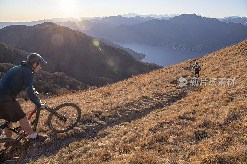骑山地车的人在日出时从长满草的山脊上骑下来