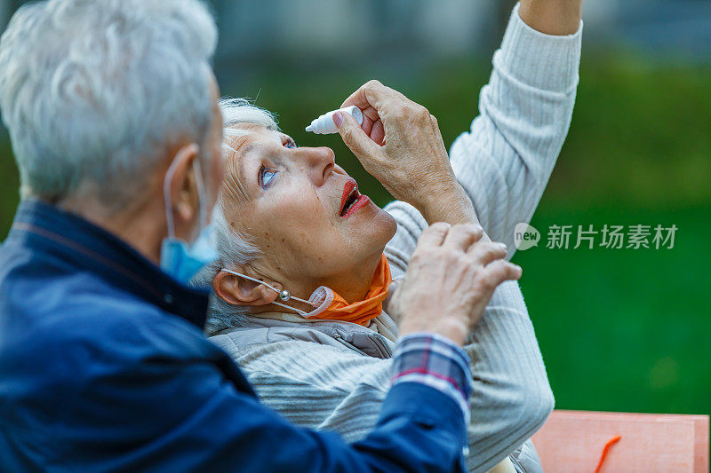 一位有眼病的老年妇女在她细心的丈夫的帮助下滴眼药水。