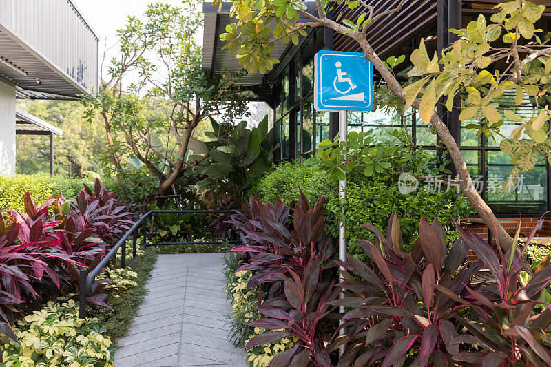 大楼前的残疾人指示牌。残疾人标志交通标志在坡道前地板上支持轮椅。在绿色自然景观的咖啡馆前的残疾人道路标志。