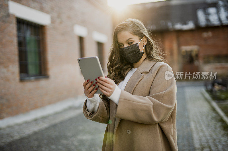 在冠状病毒大流行期间，佩戴防护口罩并在户外平板电脑上进行视频通话的妇女肖像