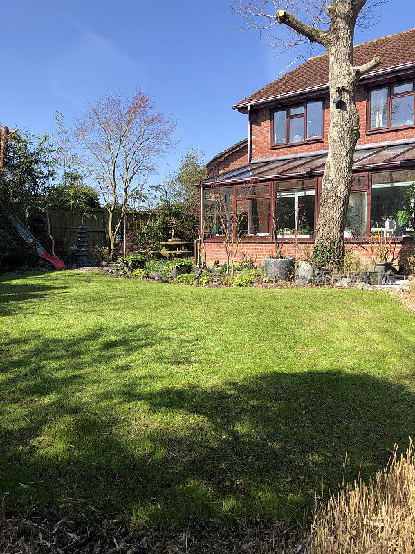 现代红砖房子的形象，温室和背阴的后花园草坪在阳光明媚的日子，清澈的蓝天