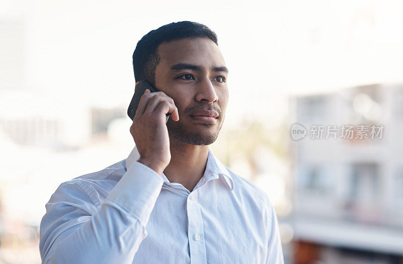 照片中，一位年轻英俊的商人独自站在办公室阳台上使用手机