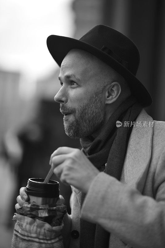 在莫斯科市中心，一名俄罗斯男子饿了，从热水瓶里吃东西。戴帽穿大衣的时髦男人。模糊的背景。黑白肖像。