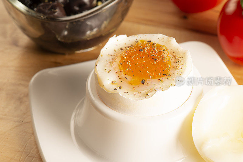 水煮鸡蛋配黑胡椒是在桌子上与橄榄和番茄的微距照片