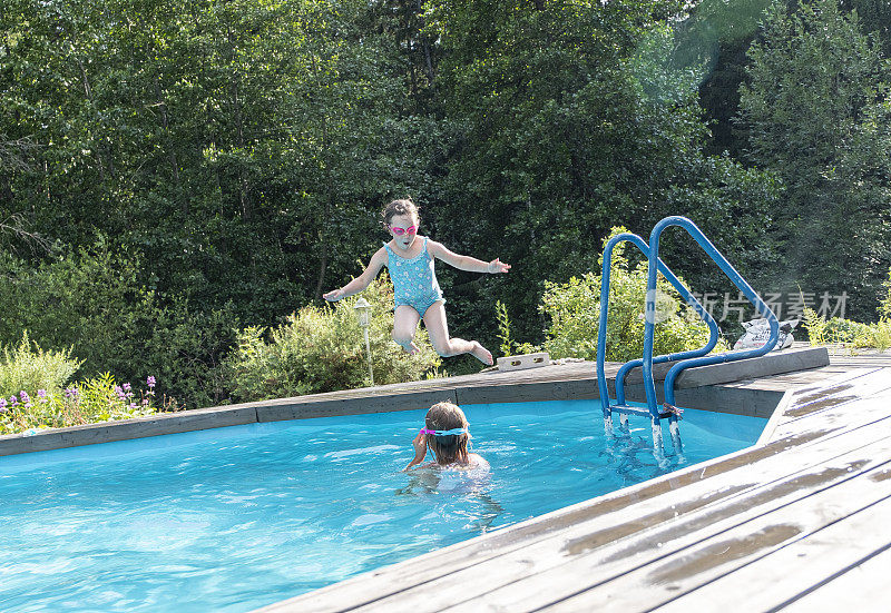 女孩们，白人女友们跳进水里。室外游泳池在房子的院子里。