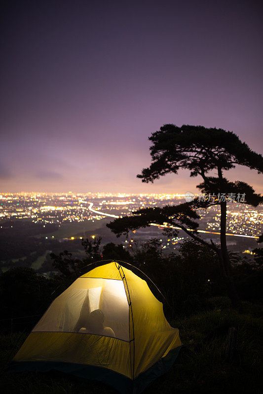 女人在帐篷里露营，在山顶俯瞰山下城市的夜景