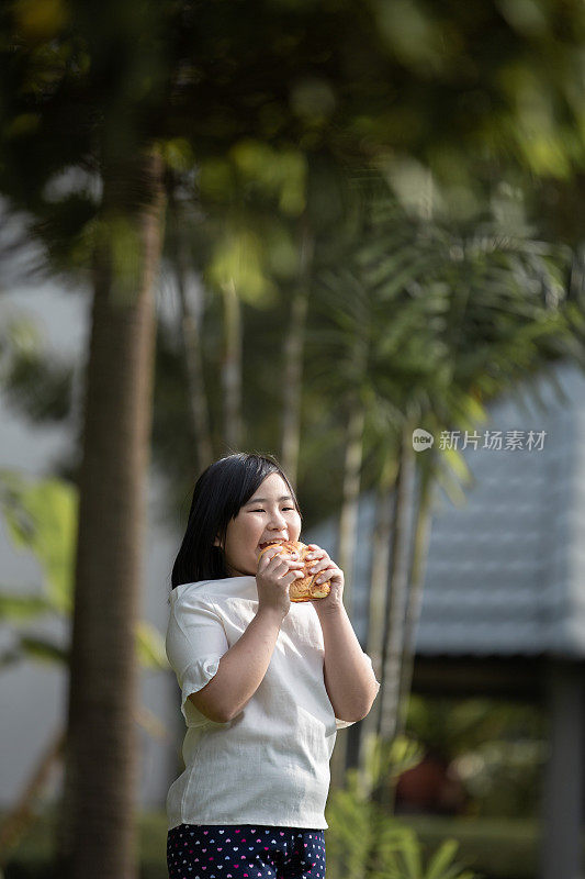 亚洲中国可爱的小女孩喜欢在阳光明媚的日子里在公园里吃她最喜欢的面包