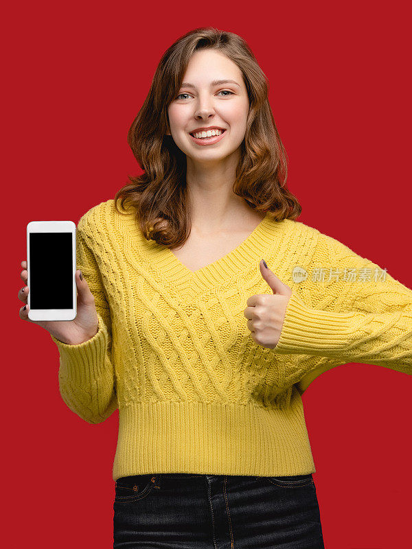 手机复制空间模板。摄影棚里的女人拿着红色背景的智能手机。概念与人空白屏的小玩意。使用广告及应用设备者
