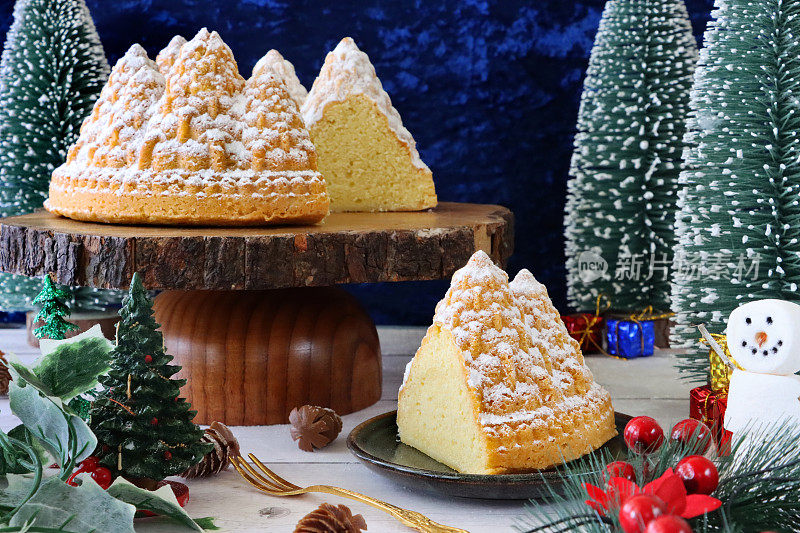 特写图片自制的切片，圣诞树形状，柠檬毛绒绒的Bundt蛋糕，柠檬味的环状海绵覆盖着糖霜，木制蛋糕架周围是圣诞树，蓝色背景