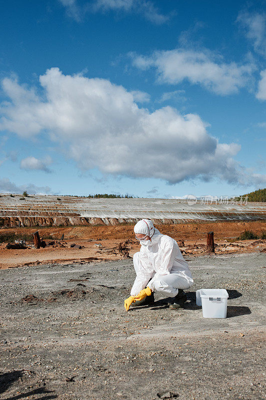 研究人员穿着防护服，戴着手套，坐在废弃区域，在研究有毒土壤时取样