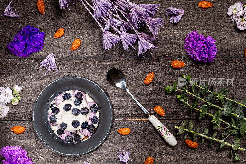 蓝莓格拉汉姆芝士蛋糕，以新鲜浆果为底，配以杏仁、紫色花朵和细枝。平的。