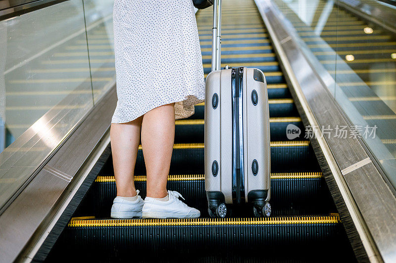 女性在机场搭乘自动扶梯。她拿着行李，准备开始一次新的旅行。