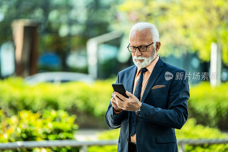 快乐的年长商人在城市街道上使用手机。